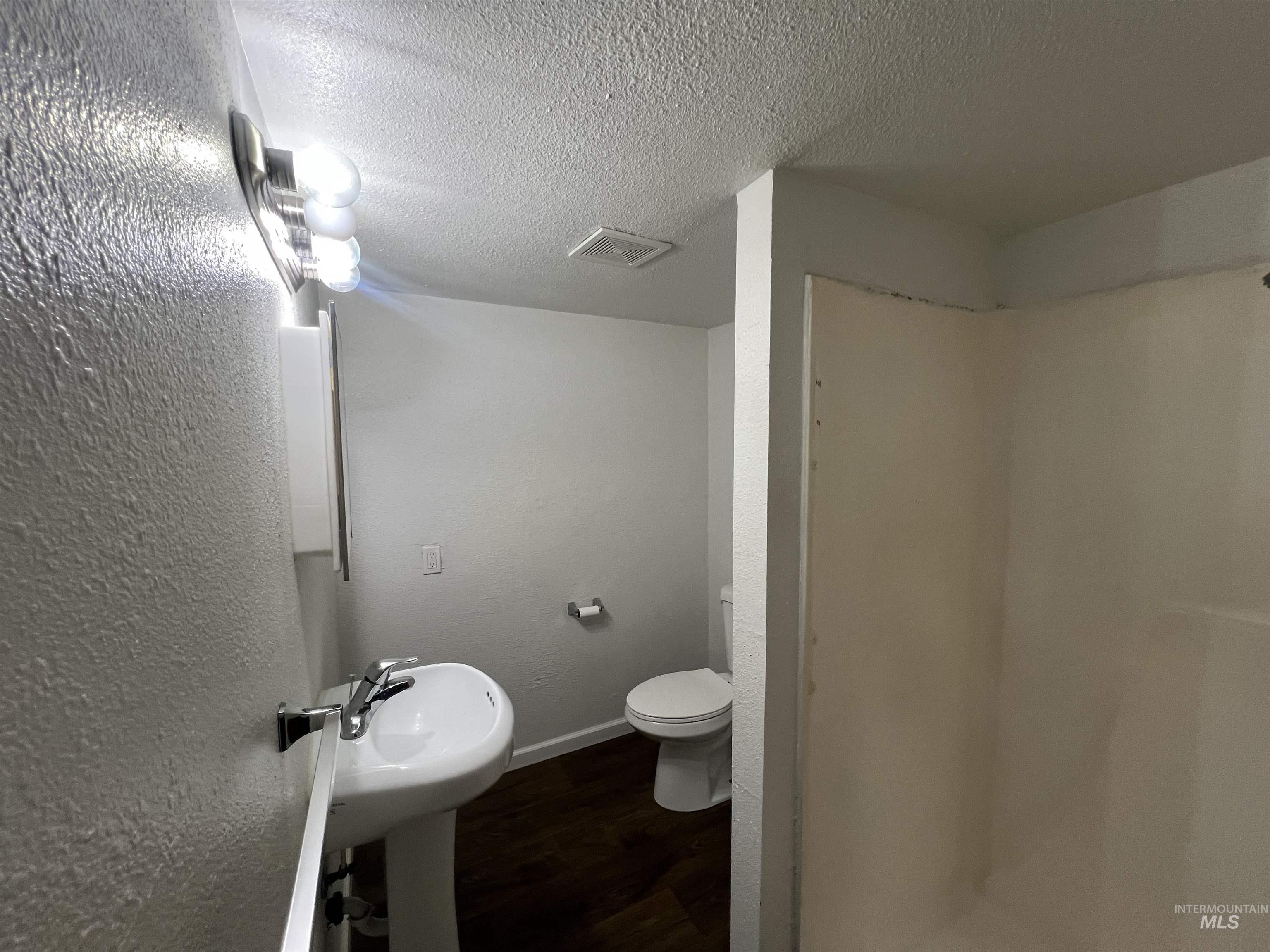 151 Northwest 8th Street Ontario, OR 97914 - Photo 15 of 30 Bathroom featuring dark wood-style floors, a textured wall, a textured ceiling, and a stall shower