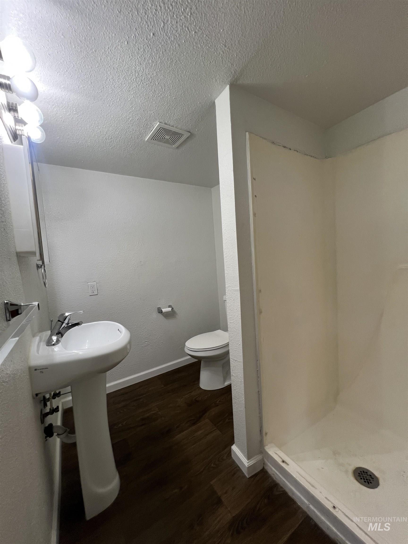 151 Northwest 8th Street Ontario, OR 97914 - Photo 19 of 30 Full bathroom featuring dark wood finished floors, a textured ceiling, a shower stall, and a textured wall