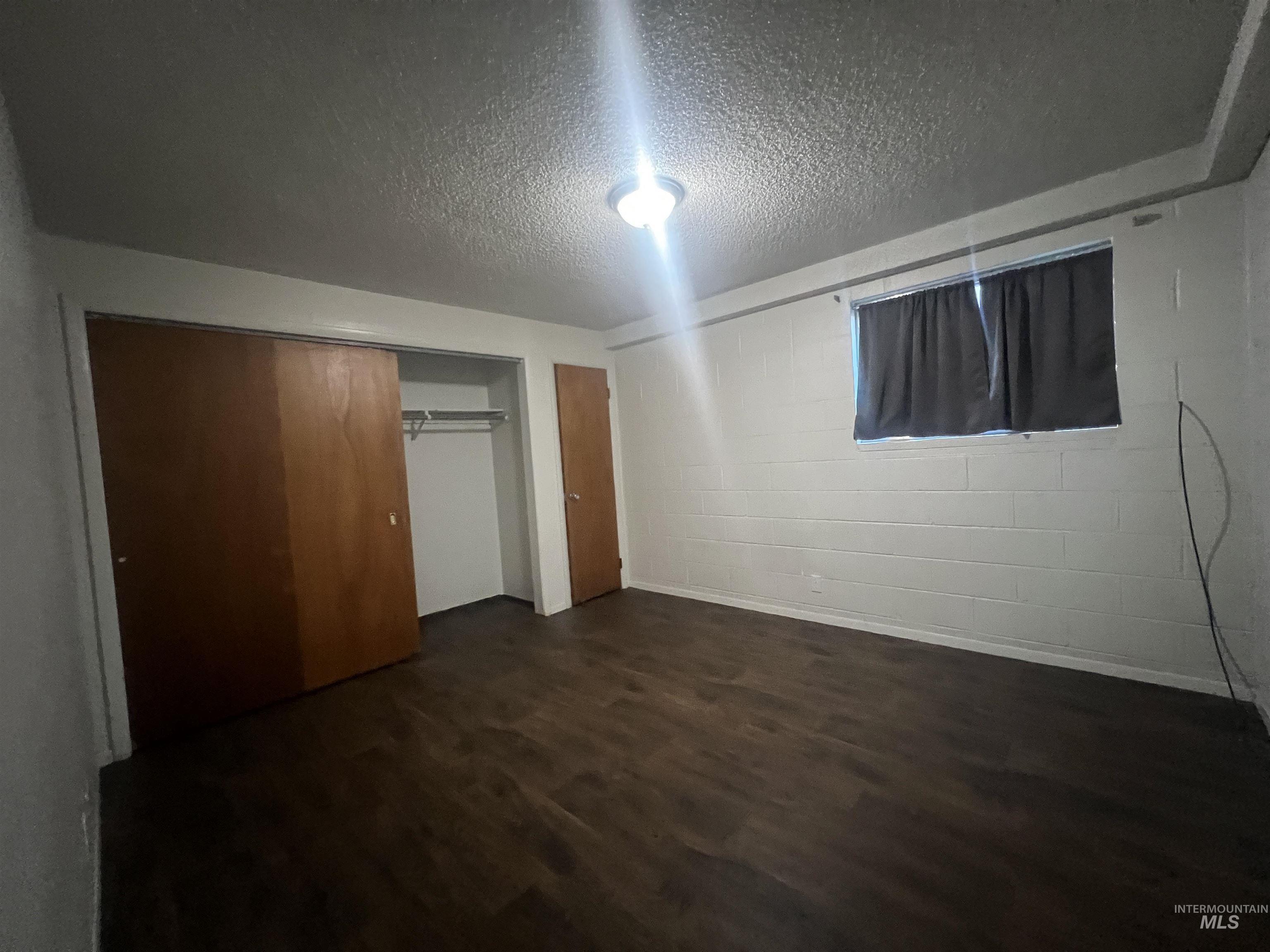 151 Northwest 8th Street Ontario, OR 97914 - Photo 28 of 30 Unfurnished bedroom featuring concrete block wall, dark wood-type flooring, a textured ceiling, and a closet