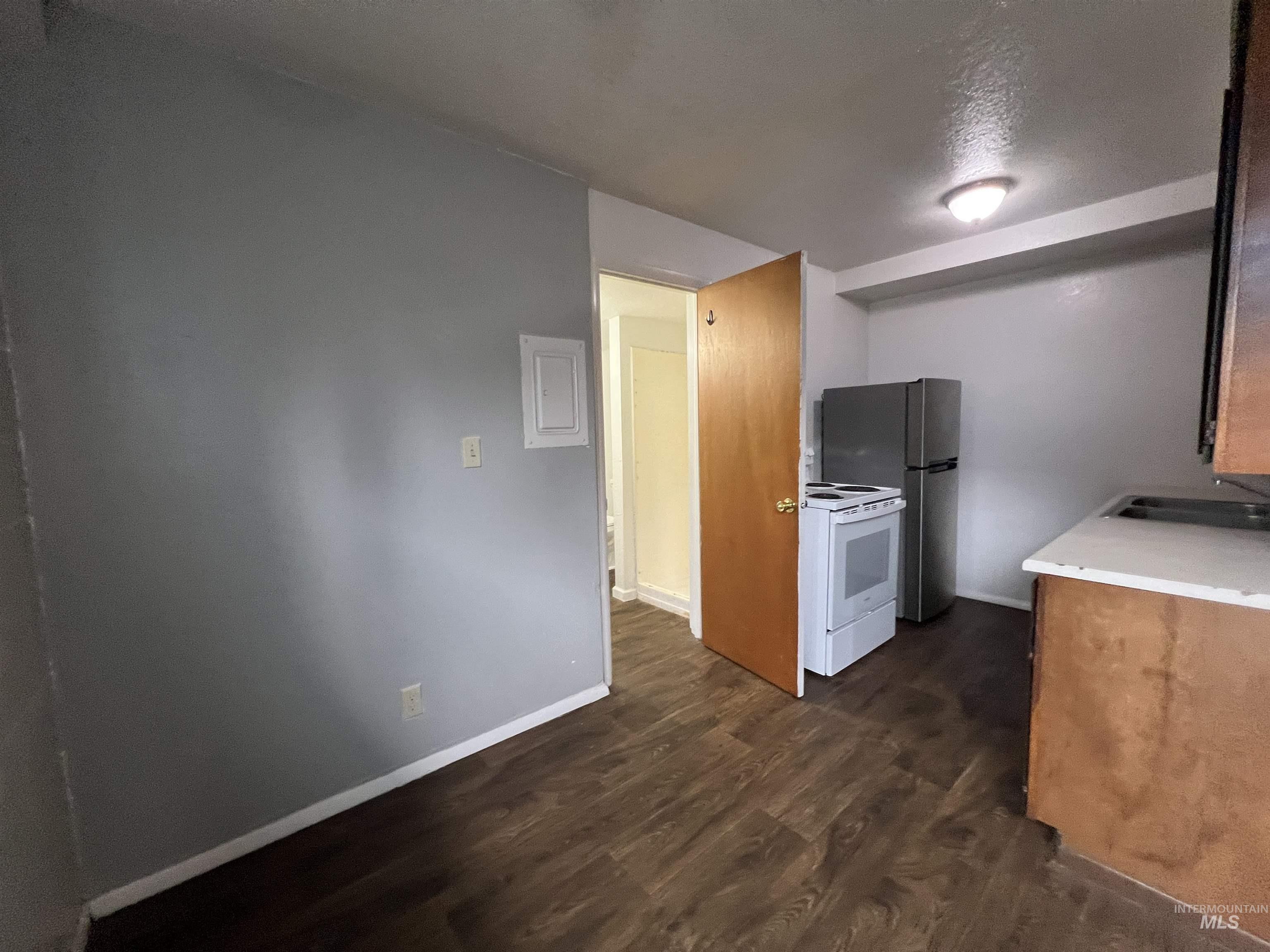 151 Northwest 8th Street Ontario, OR 97914 - Photo 6 of 30 Kitchen with light countertops, dark wood-style flooring, white appliances, electric panel, and brown cabinets