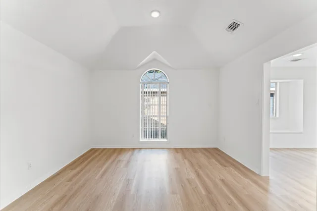 an empty room with wooden floor chandelier and windows