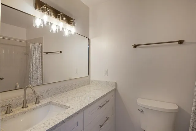 a bathroom with a granite countertop sink a toilet and a mirror