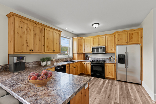 75 East 200 North Mendon, UT 84325 - Photo 8 of 36 Kitchen with black appliances, a kitchen bar, a peninsula, light wood-style flooring, and light wood finish cabinetry