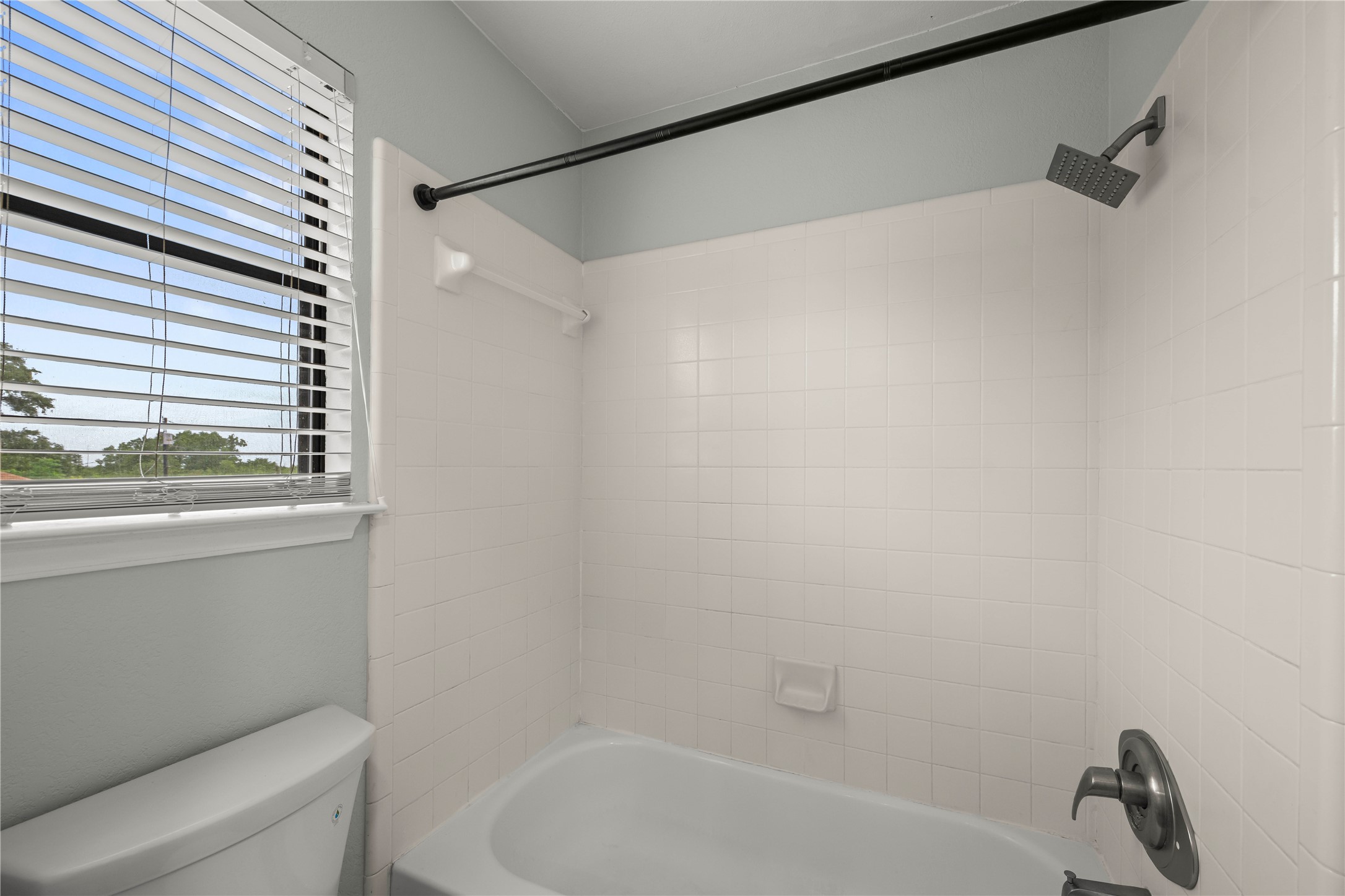 1329 Quail Ravine Round Rock, TX 78664 - Photo 24 of 39 A classic shower and tub combination rests adjacent to a window with horizontal blinds.
