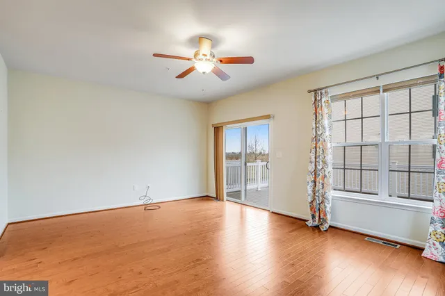 an empty room with wooden floor fan and windows