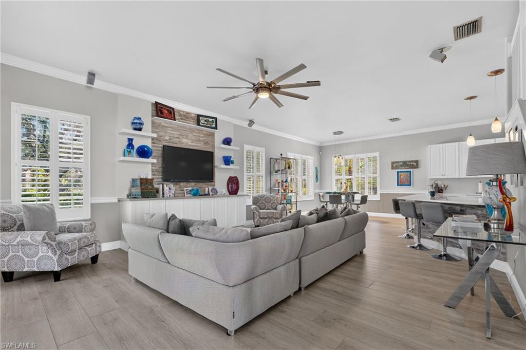 9970 Rookery Circle Estero, FL 33928 - Photo 6 of 50 Open-concept living area featuring wood-finish flooring, a ceiling fan, built-in shelving, white plantation shutters, and a kitchen island with seating