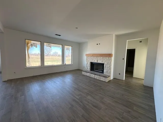 an empty room with wooden floor fireplace and windows