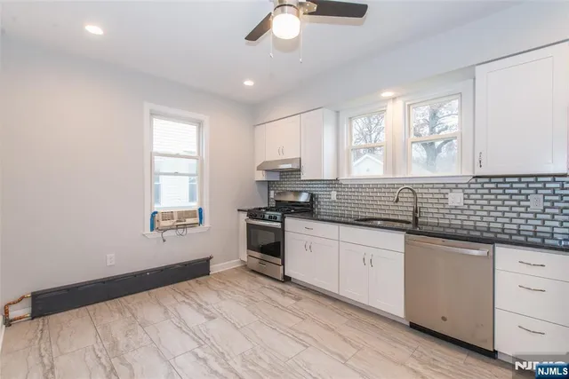 a kitchen with granite countertop a stove a sink and white cabinets with wooden floor