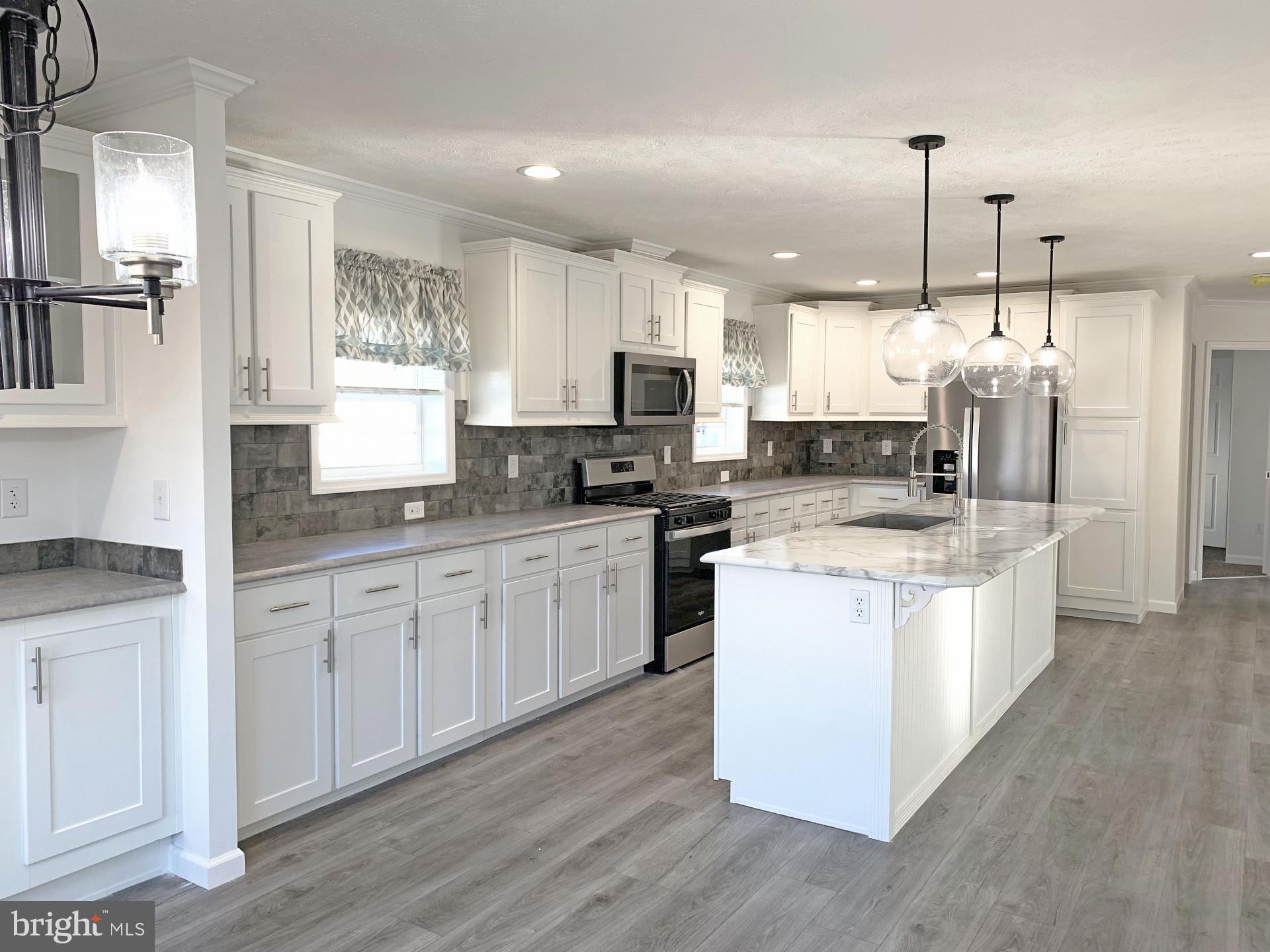 a large kitchen with stainless steel appliances kitchen island granite countertop a stove a sink a refrigerator and white cabinets with wooden floor
