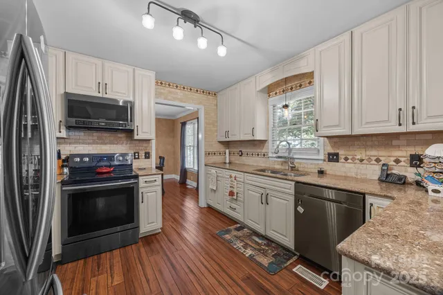 a kitchen with stainless steel appliances granite countertop a stove a sink dishwasher a refrigerator and a microwave oven with wooden floor