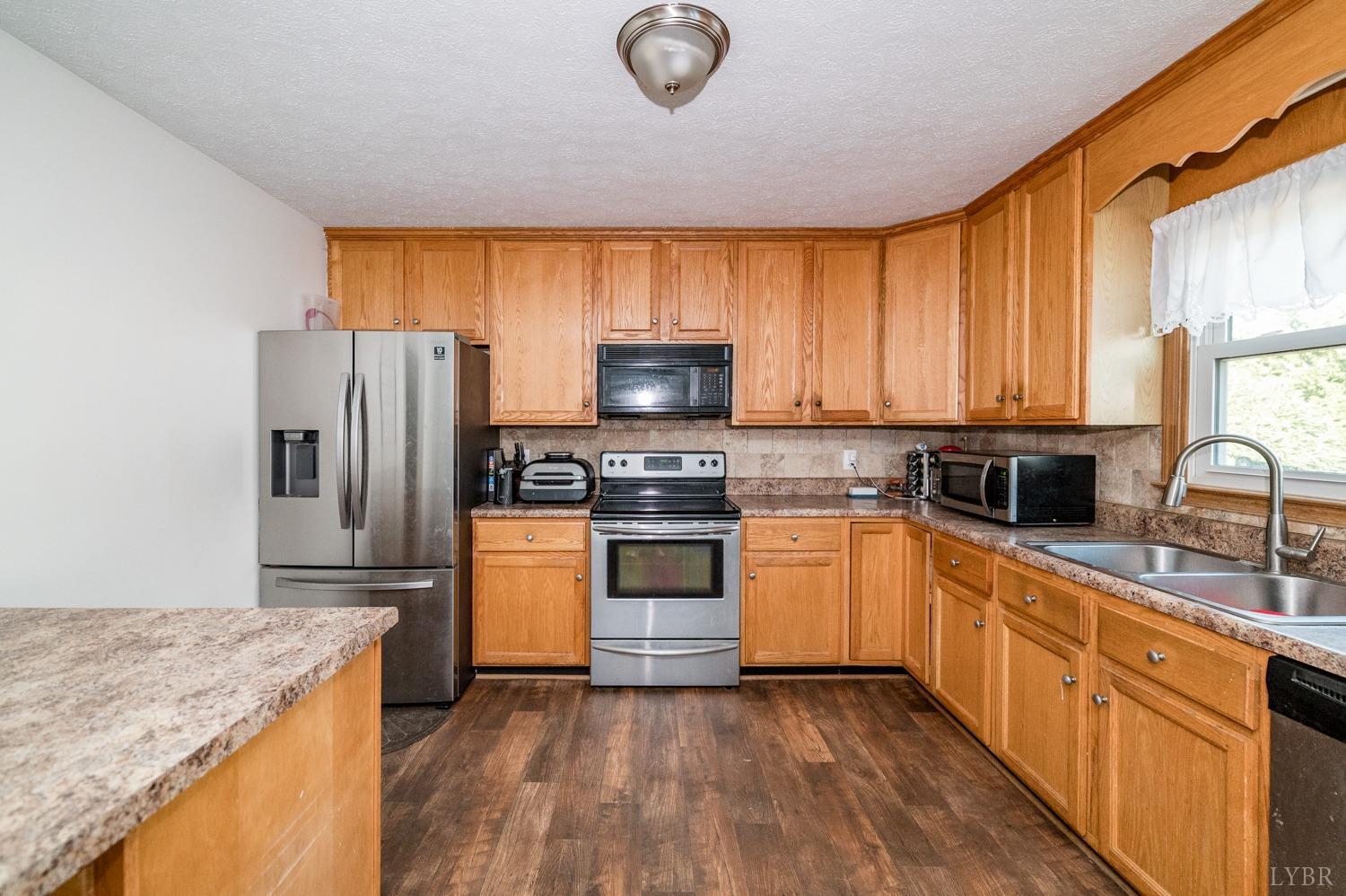 2271 Sunburst Road Evington, VA 24550 - Photo 4 of 26 a kitchen with granite countertop a stove top oven a sink dishwasher a refrigerator and a microwave oven with wooden floor