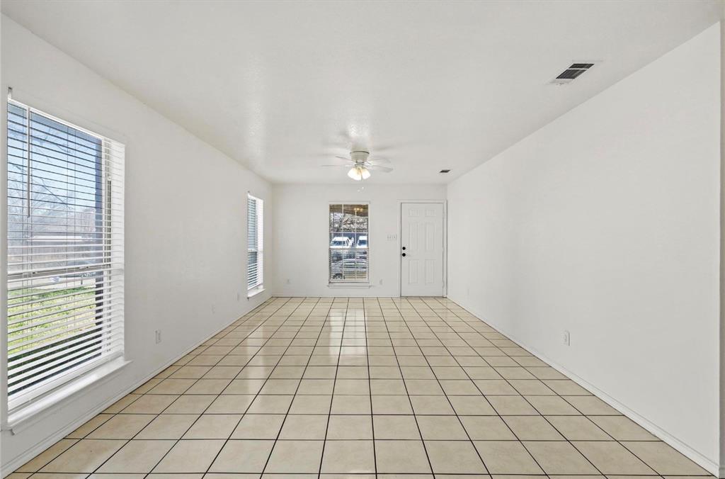 5169 East Rim Road Dallas, TX 75211 - Photo 10 of 19 Spacious room featuring light-toned tile flooring, multiple windows with blinds, a ceiling fan, and a paneled entry door
