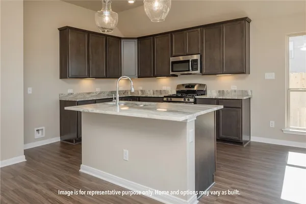 a view of an empty room with wooden floor and a kitchen