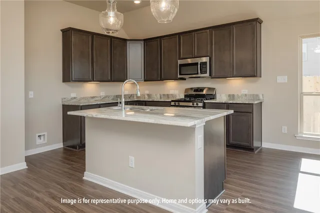 a view of an empty room with wooden floor and a kitchen