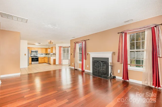 a view of an empty room with wooden floor fireplace and a window