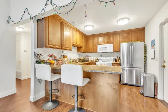 a kitchen with stainless steel appliances granite countertop a refrigerator a stove a sink dishwasher and white cabinets with wooden floor