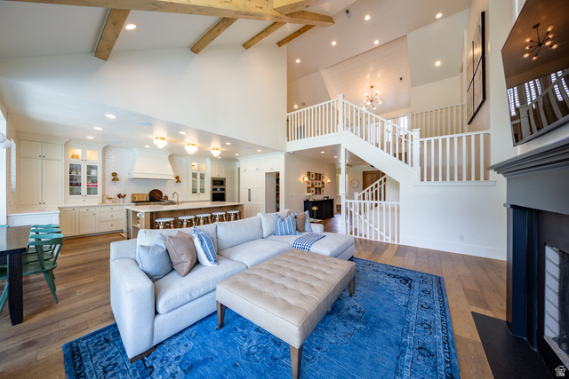 630 East Center Street Alpine, UT 84004 - Photo 39 of 115 Vaulted ceiling with exposed wood beams, wood-finish flooring, built-in kitchen cabinetry with glass panel accents, multi-level staircase with white railings, and a fireplace with a dark mantel