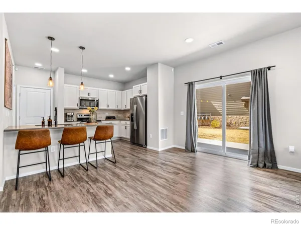 a living room with kitchen view and a refrigerator with wooden floor