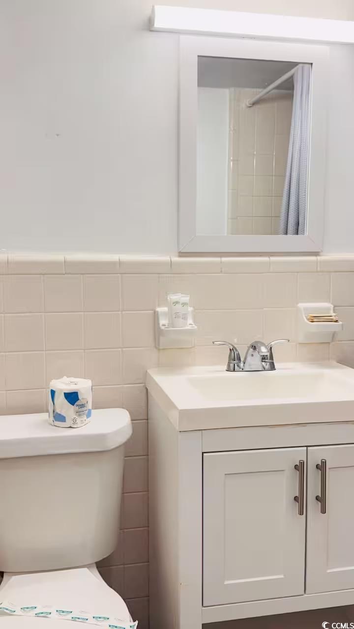 1600 South Ocean Boulevard, Unit 322 Myrtle Beach, SC 29577 - Photo 11 of 16 Bathroom featuring a shower with shower curtain, vanity, wainscoting, and tile walls