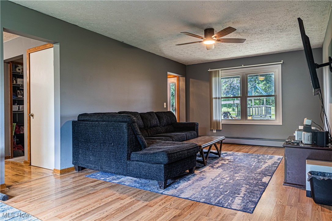 16974 Hawley Road Oberlin, OH 44074 - Photo 11 of 42 Living room with light wood finished floors, a textured ceiling, a ceiling fan, and a baseboard heating unit