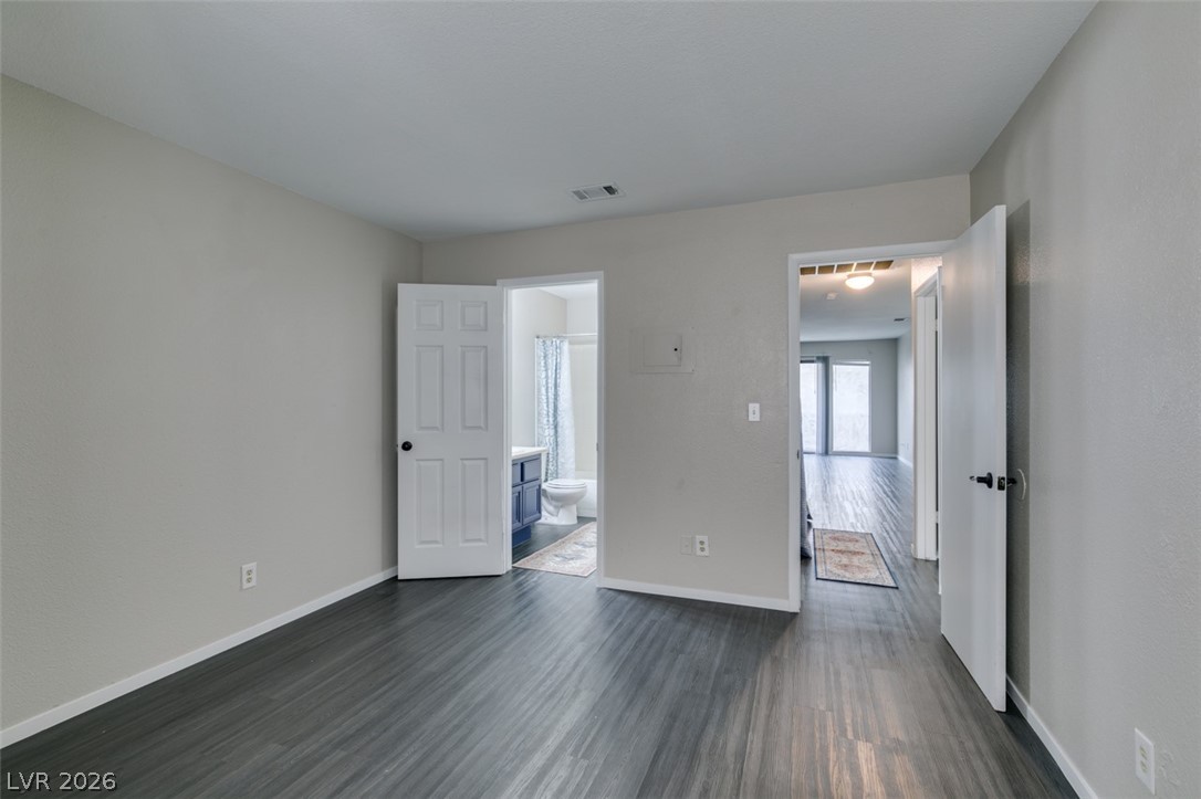 810 North Sloan Lane, Unit 103 Las Vegas, NV 89110 - Photo 8 of 16 Unfurnished bedroom featuring dark wood-style flooring, baseboards, and connected bathroom