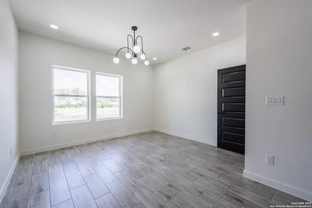 an empty room with wooden floor chandelier and windows