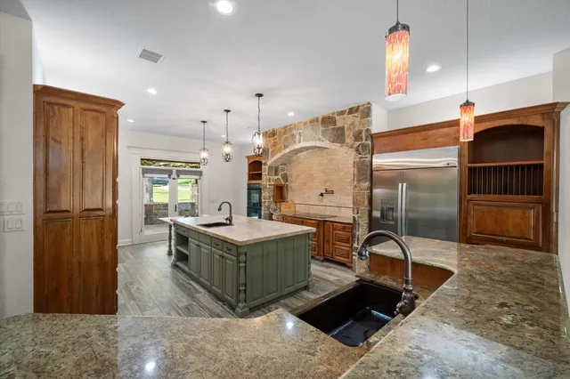 a kitchen with stainless steel appliances kitchen island granite countertop a refrigerator and a sink