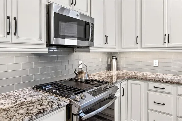 a kitchen with granite countertop a stove and a white cabinets
