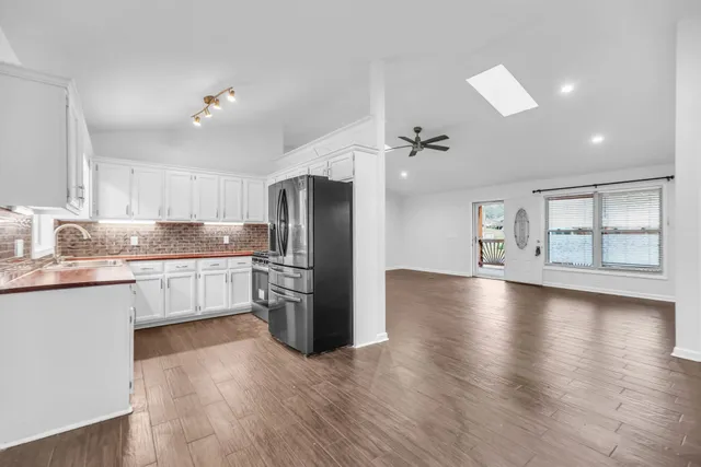 a kitchen with stainless steel appliances granite countertop a refrigerator a sink dishwasher a stove and white countertops with wooden floor