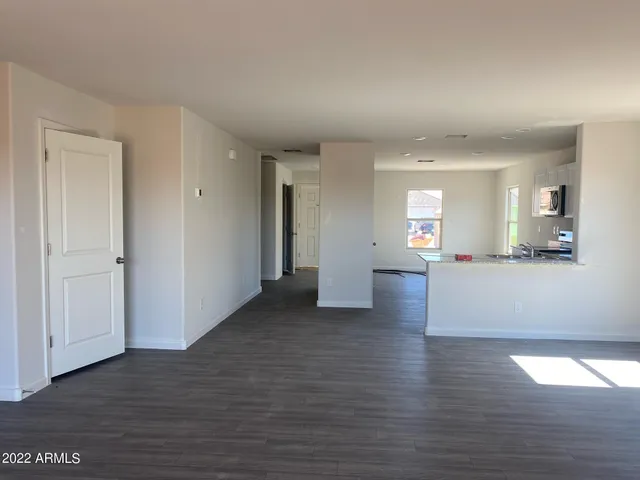 a view of an empty room with wooden floor and a kitchen