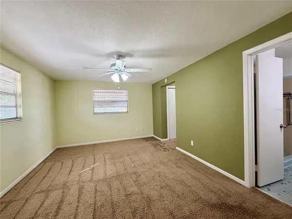 an empty room with chandelier fan and windows