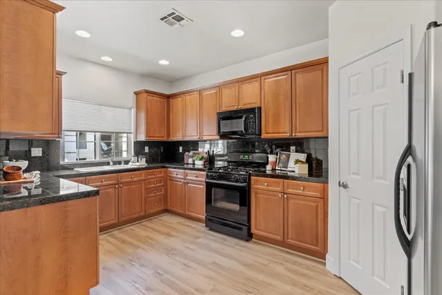 a kitchen with stainless steel appliances granite countertop a refrigerator a sink dishwasher a stove and white cabinets with wooden floor