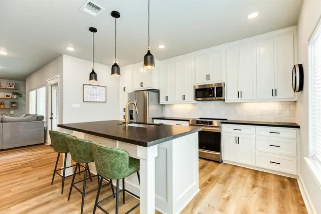 a kitchen with stainless steel appliances granite countertop a stove a sink a microwave a refrigerator and white cabinets with wooden floor