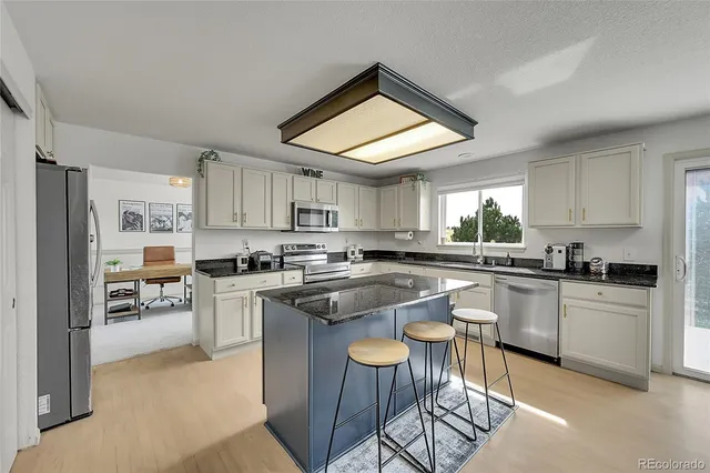 a kitchen with stainless steel appliances granite countertop a stove top oven a sink a refrigerator and white cabinets