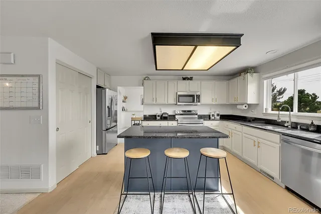 a kitchen with stainless steel appliances granite countertop a refrigerator a sink dishwasher a dining table and chairs with wooden floor