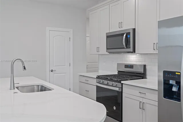 a kitchen with white cabinets a sink stove and microwave