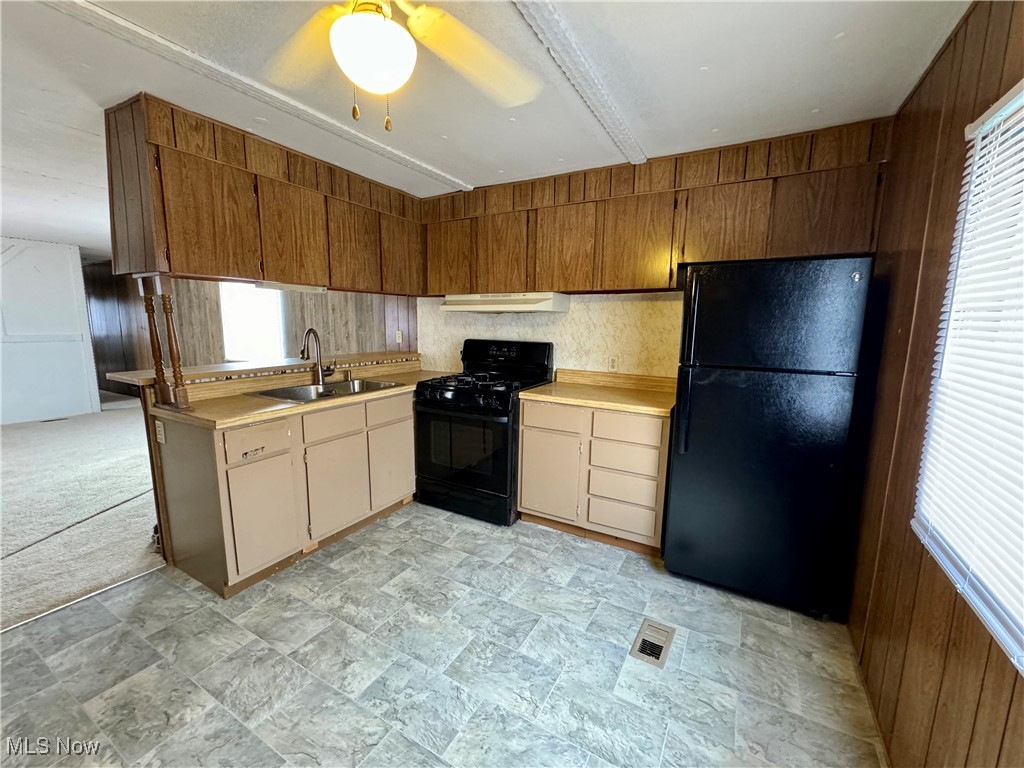 Kitchen featuring sink, light colored carpet, wood walls, and black appliances