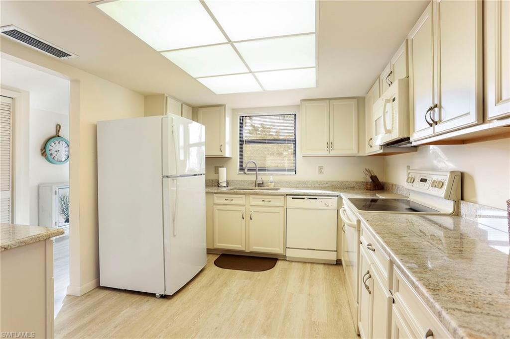 95 St Andrews Boulevard, Unit B209 Naples, FL 34113 - Photo 11 of 18 a kitchen with a refrigerator a stove a sink dishwasher and wooden cabinets with wooden floor