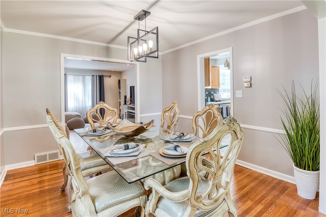 4520 Birchwold Road Cleveland, OH 44121 - Photo 9 of 40 Dining room featuring light wood-type flooring, elegant glass table, chandelier and ornamental molding
