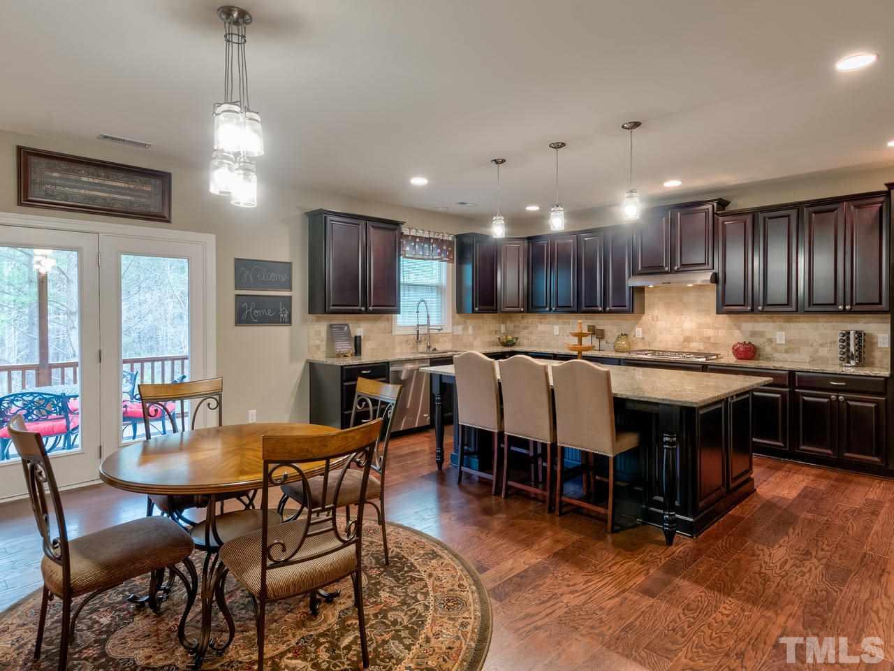 8325 Henderson Road Apex, NC 27539 - Photo 5 of 29 a kitchen with stainless steel appliances granite countertop a stove top oven a refrigerator a sink and a dining table with chairs