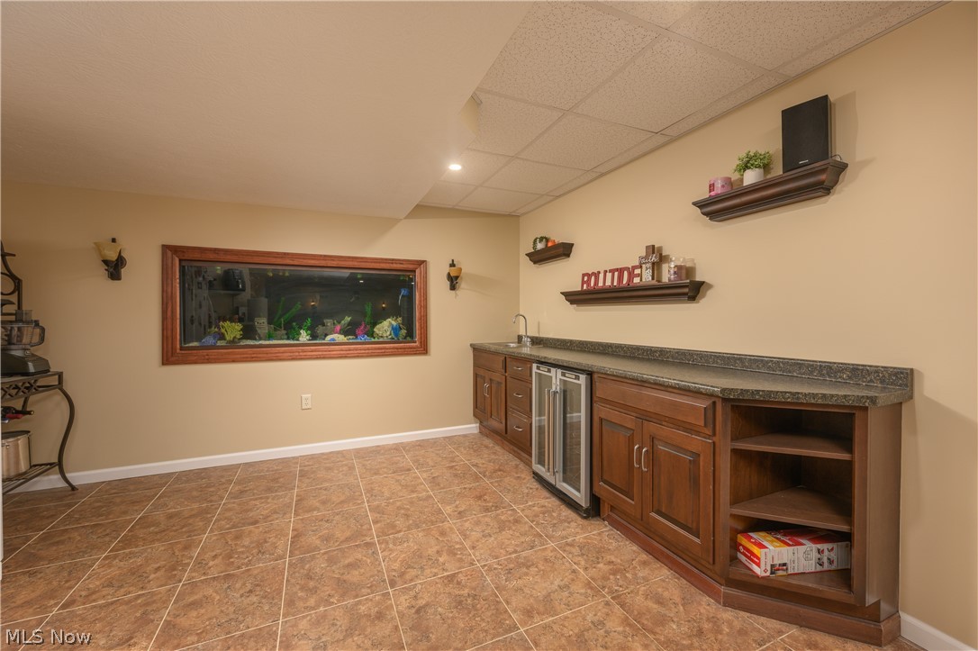 806 Forrest Ridge Drive Dover, OH 44622 - Photo 32 of 36 Indoor wet bar with open shelves, dark countertops, beverage cooler, a paneled ceiling, and wood finish cabinets