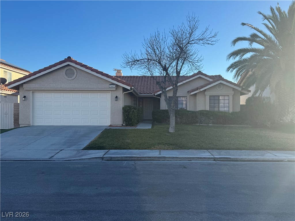 Ranch-style home featuring a tiled roof, a front yard, driveway, a garage, and stucco siding