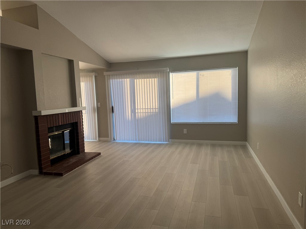 7447 Palermo Avenue Las Vegas, NV 89147 - Photo 4 of 26 Unfurnished living room with light wood-style flooring, vaulted ceiling, and a brick fireplace