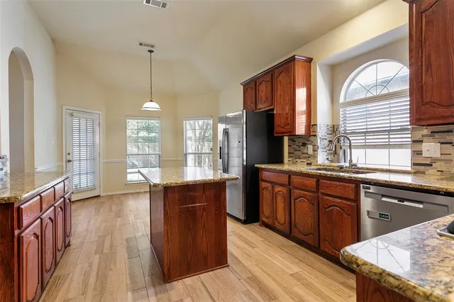 a kitchen with stainless steel appliances granite countertop wooden floors a sink and a window