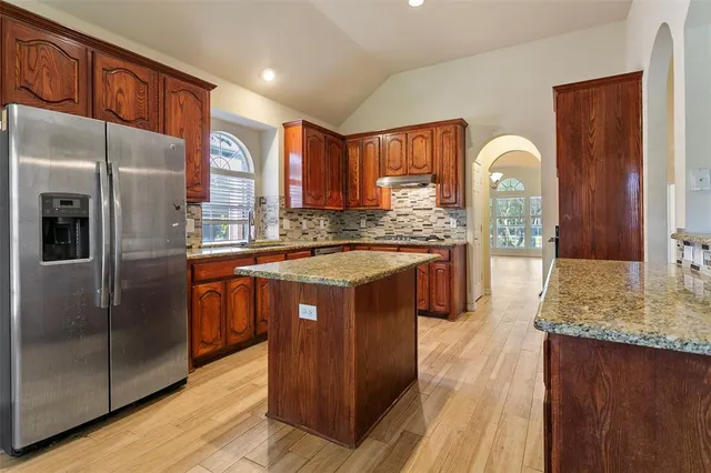 a kitchen with stainless steel appliances granite countertop a refrigerator a sink and a wooden cabinets