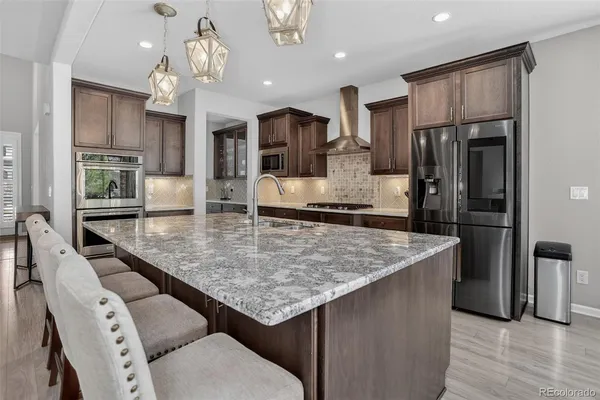 a kitchen with stainless steel appliances granite countertop a kitchen island a stove a refrigerator a oven a dining table and chairs with wooden floor