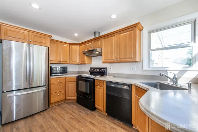 a kitchen with granite countertop stainless steel appliances a sink a refrigerator a window and cabinets