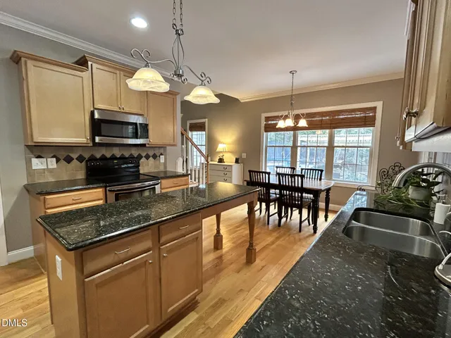 a kitchen with stainless steel appliances granite countertop a stove top oven a sink a dining table and chairs with wooden floor