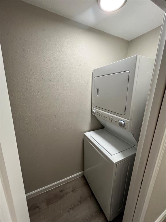 7046 Forney Road Dallas, TX 75227 - Photo 9 of 19 Dedicated laundry area featuring a stacked washer and dryer unit, wood-finish flooring, neutral wall tones, white baseboards, and a flush-mount ceiling light
