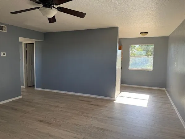 an empty room with wooden floor fan and windows